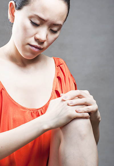 Photo of a woman in a orange shirt holding her knee.