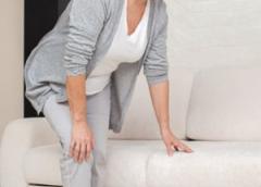 Photo of a woman having trouble getting up from a couch due to knee pain.