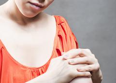 Photo of a woman in a orange shirt holding her knee.