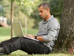 man using a laptop while sitting beneath a tree